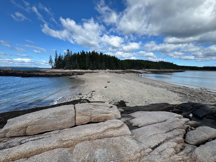 sand bar connecting two pieces of land, blue skies with cumulous clouds