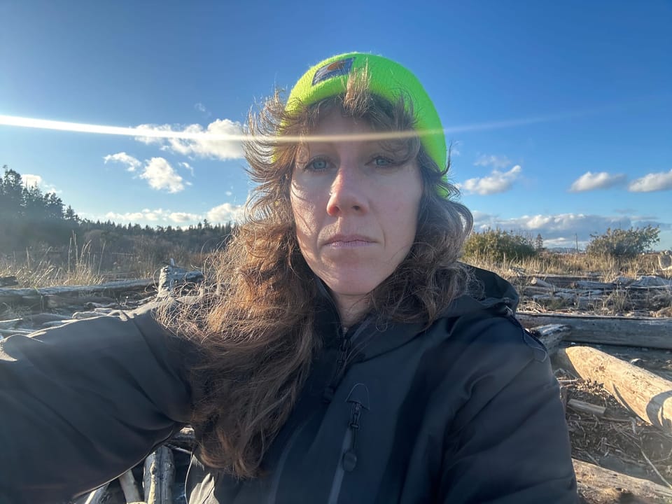 photo of white femme wearing neon yellow beanie, on a beach